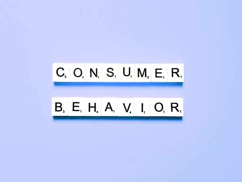 The image shows the words "CONSUMER BEHAVIOR" spelled out using individual Scrabble-style letter tiles. Each letter tile has a corresponding Scrabble score number at the bottom right, arranged neatly in two rows on a light blue background. The first row spells "CONSUMER," and the second row spells "BEHAVIOR." The overall composition is clean and minimalistic, with the focus being on the text and tiles.
