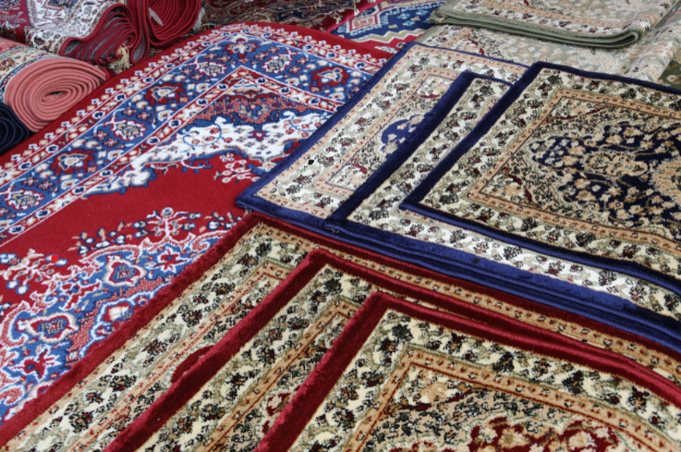 A collection of traditional rugs in various patterns and vibrant colors, including red, blue, and beige tones. The rugs display intricate floral and geometric designs, highlighting the detailed craftsmanship and variety of styles commonly found in classic rug collections.