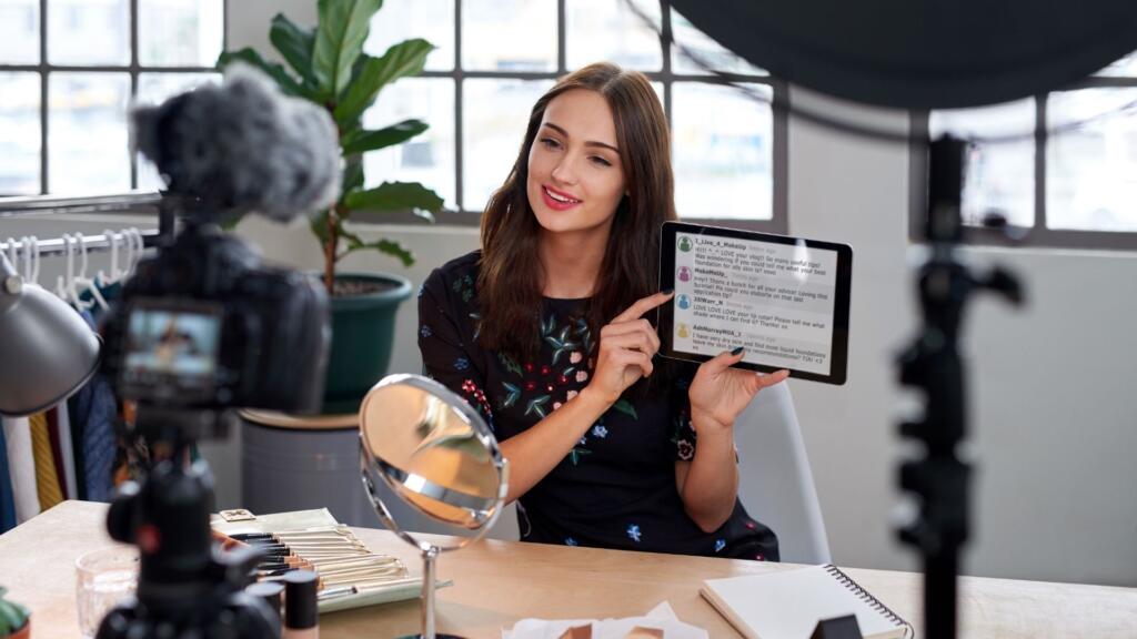 A content creator filming herself holding a tablet, displaying comments, while recording a video for social media, set in a bright studio environment.






