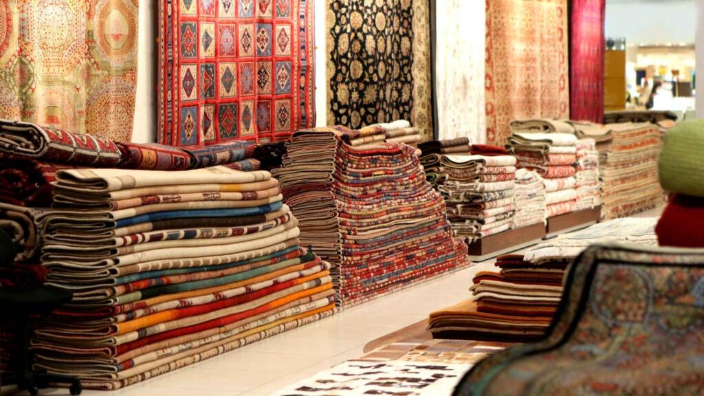 Stacks of traditional rugs in a showroom, featuring a wide variety of colors and intricate patterns, showcasing the diverse selection available for home decor.






