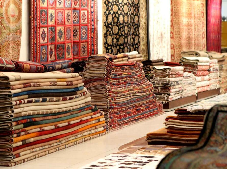 Stacks of traditional rugs in a showroom, featuring a wide variety of colors and intricate patterns, showcasing the diverse selection available for home decor.