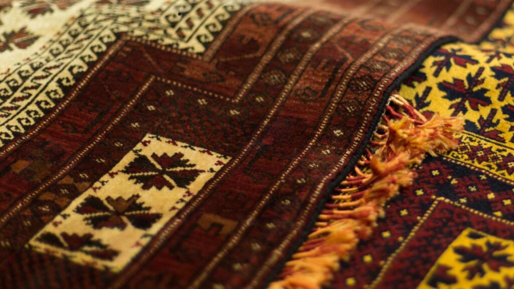 Close-up of a traditional woven rug with intricate geometric patterns in rich red, cream, and yellow hues, featuring tassels along the edge for a classic handcrafted look.