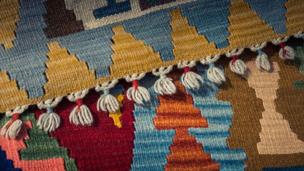 Close-up view of a colorful woven rug with intricate geometric patterns and decorative tassels, highlighting its craftsmanship and vibrant design.