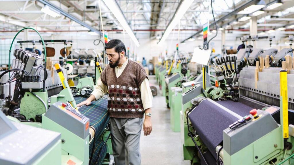 A worker inspecting a pile of finished textiles in a well-lit and organized factory, highlighting ethical labor practices and safe working conditions.