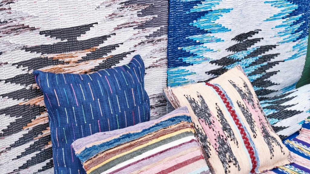 A collection of colorful, handwoven rugs and pillows made from sustainable fabrics.