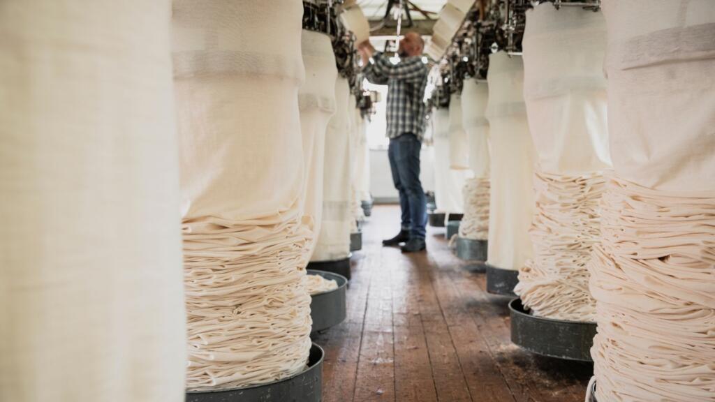 A worker inspecting a pile of finished textiles in a well-lit and organized factory, highlighting ethical labor practices and safe working conditions.
