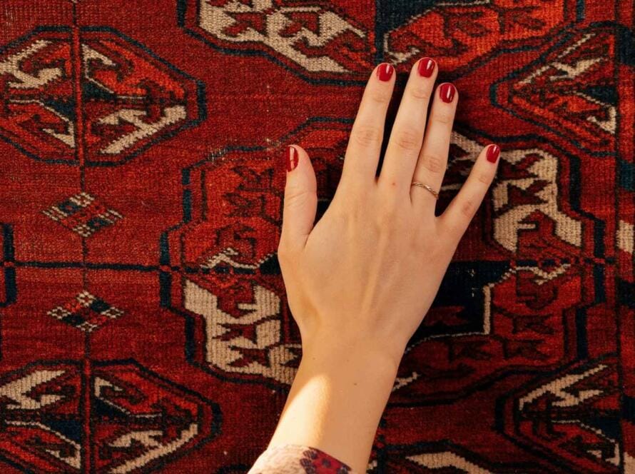 "Hand gently touching a traditional Turkish rug with a red geometric design showcasing its fine texture"
