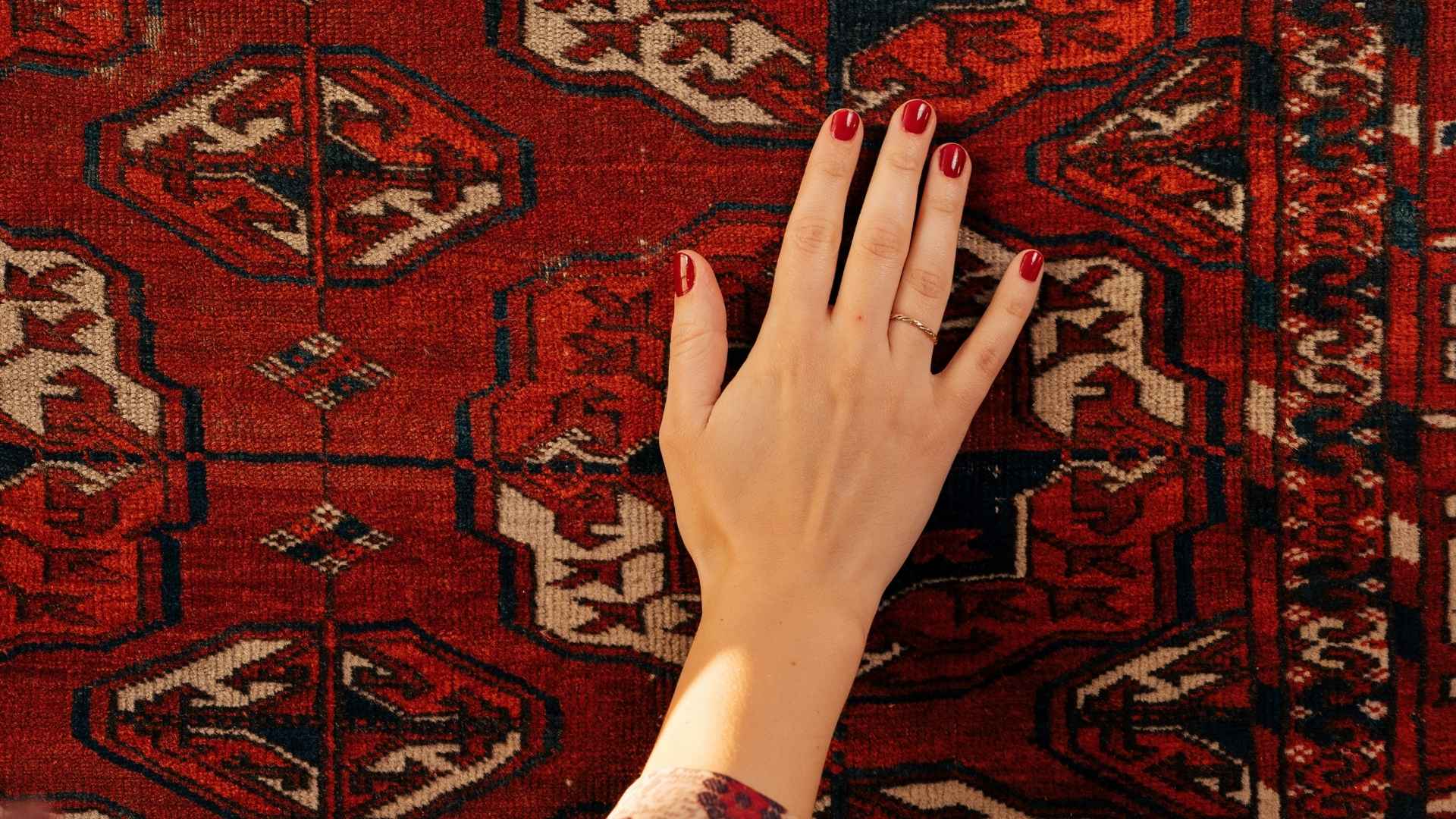 "Hand gently touching a traditional Turkish rug with a red geometric design showcasing its fine texture"