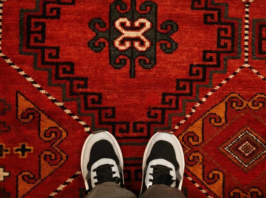 Feet standing on a bold red carpet with striking geometric designs, highlighting the unique style and comfort from American Carpet Wholesalers.