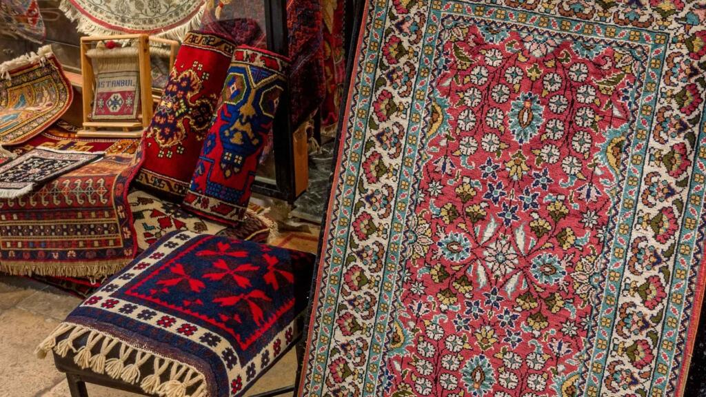 A variety of colorful, handwoven rugs and pillows displayed in a market stall.
