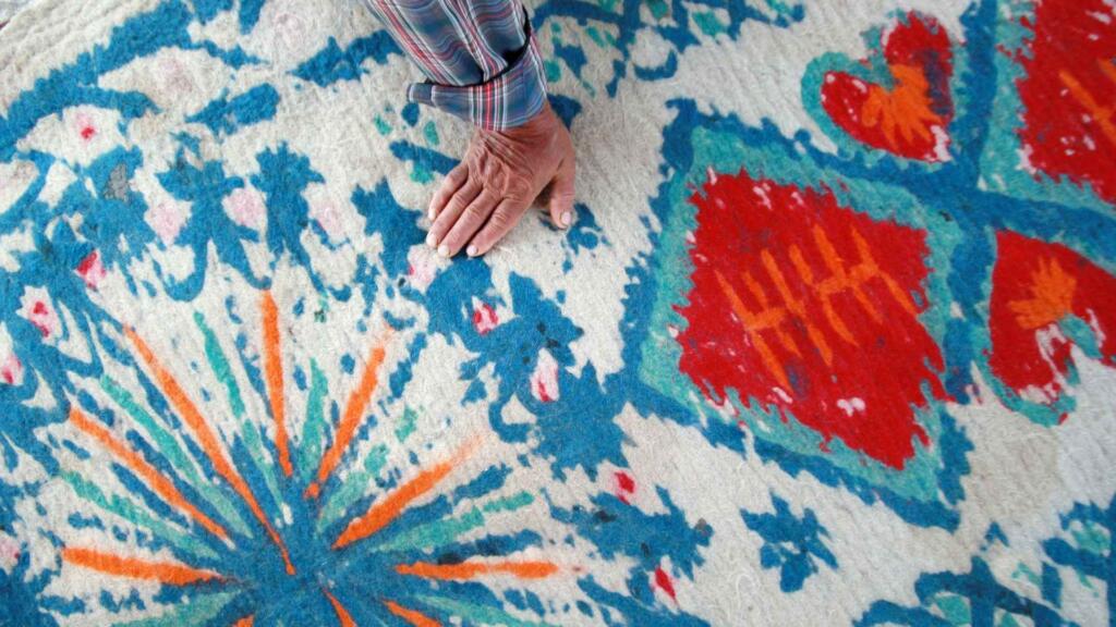 A hand resting on a colorful, handwoven rug with intricate patterns.