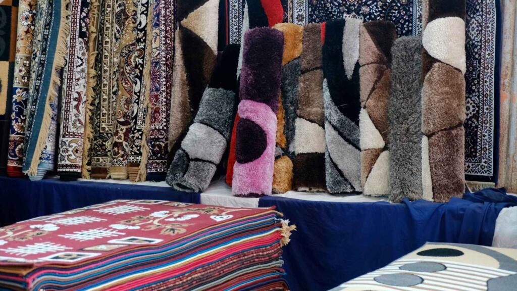 Display of various colorful and textured custom carpets and rugs in a store, showcasing diverse patterns and styles