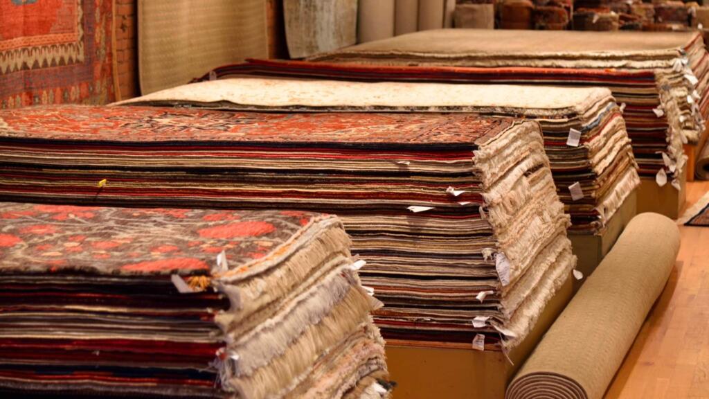 Stacks of intricately designed rugs in a showroom, showcasing a variety of colors, patterns, and textures.