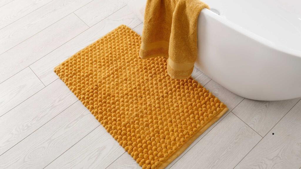 Yellow bath mat on a wooden floor next to a bathtub.