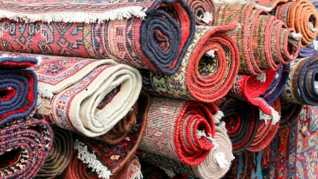 Neatly stacked rolls of colorful, intricately woven rugs and carpets, featuring traditional patterns and vibrant designs for wholesale.