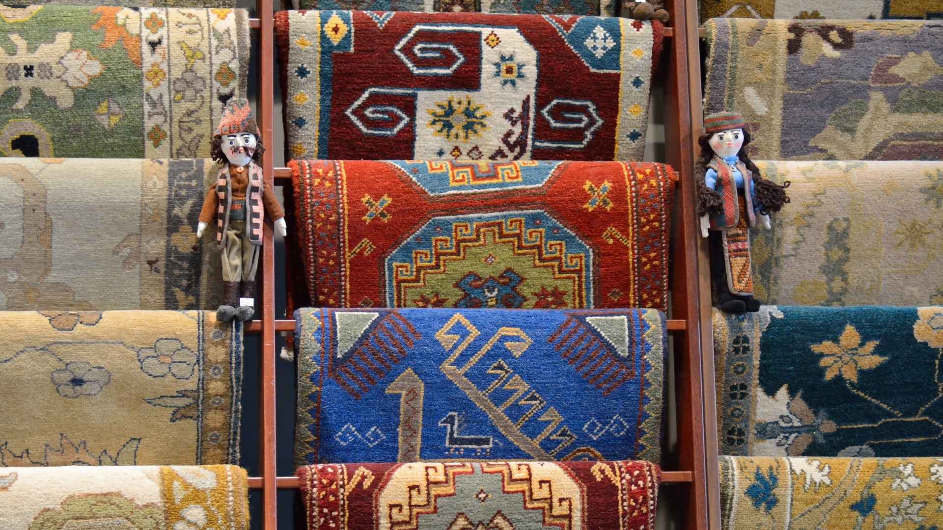 Display of colorful, intricately designed carpets and rugs by wholesalers, adorned with traditional patterns and cultural details