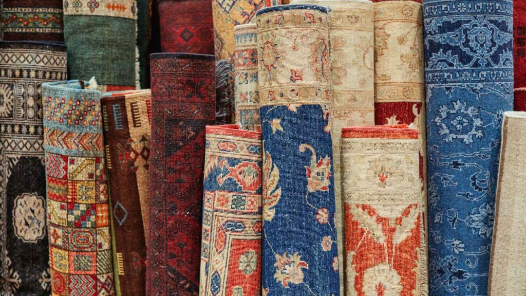 Stacked rolls of beautifully patterned carpets and rugs in a variety of colors and traditional designs, available at wholesale.