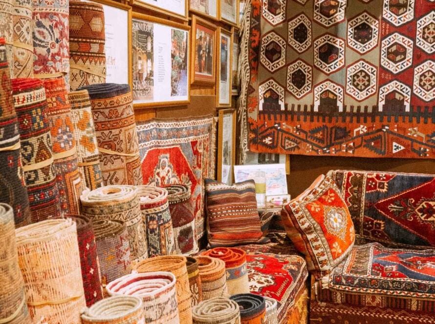 Close-up of rolled and layered Persian-style carpets featuring intricate floral and geometric designs, perfect for retail shops.