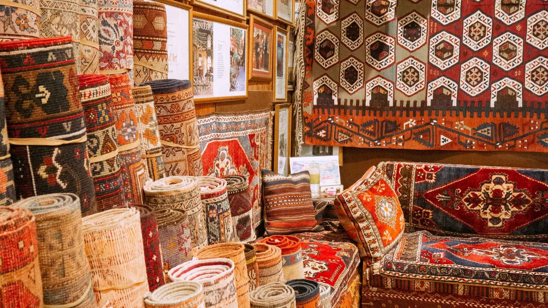 Close-up of rolled and layered Persian-style carpets featuring intricate floral and geometric designs, perfect for retail shops.