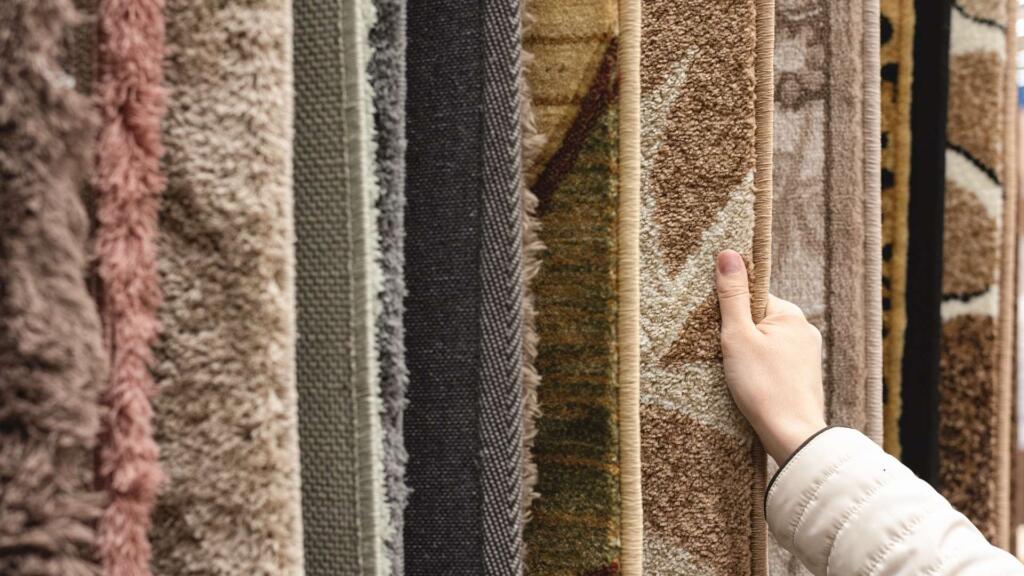 A variety of custom shape carpets in different textures and patterns displayed vertically, with a person touching one of the designs.