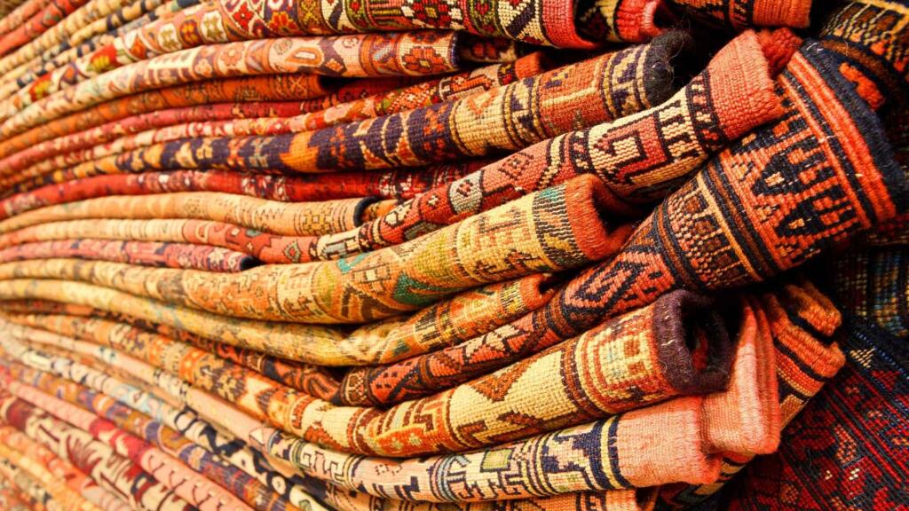 A close-up view of stacked custom shape carpets in rich, intricate designs with warm, earthy tones.