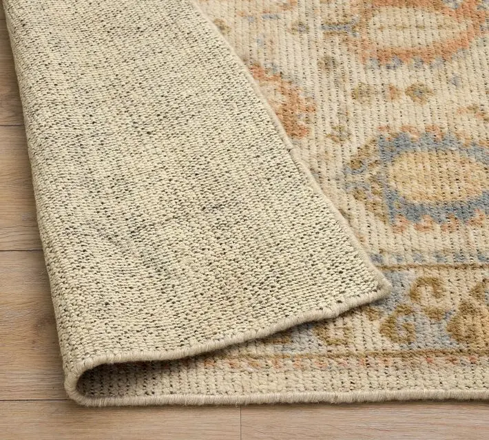 A beige woven rug with a subtle pattern, flipped to show its underside, on a light wood floor.