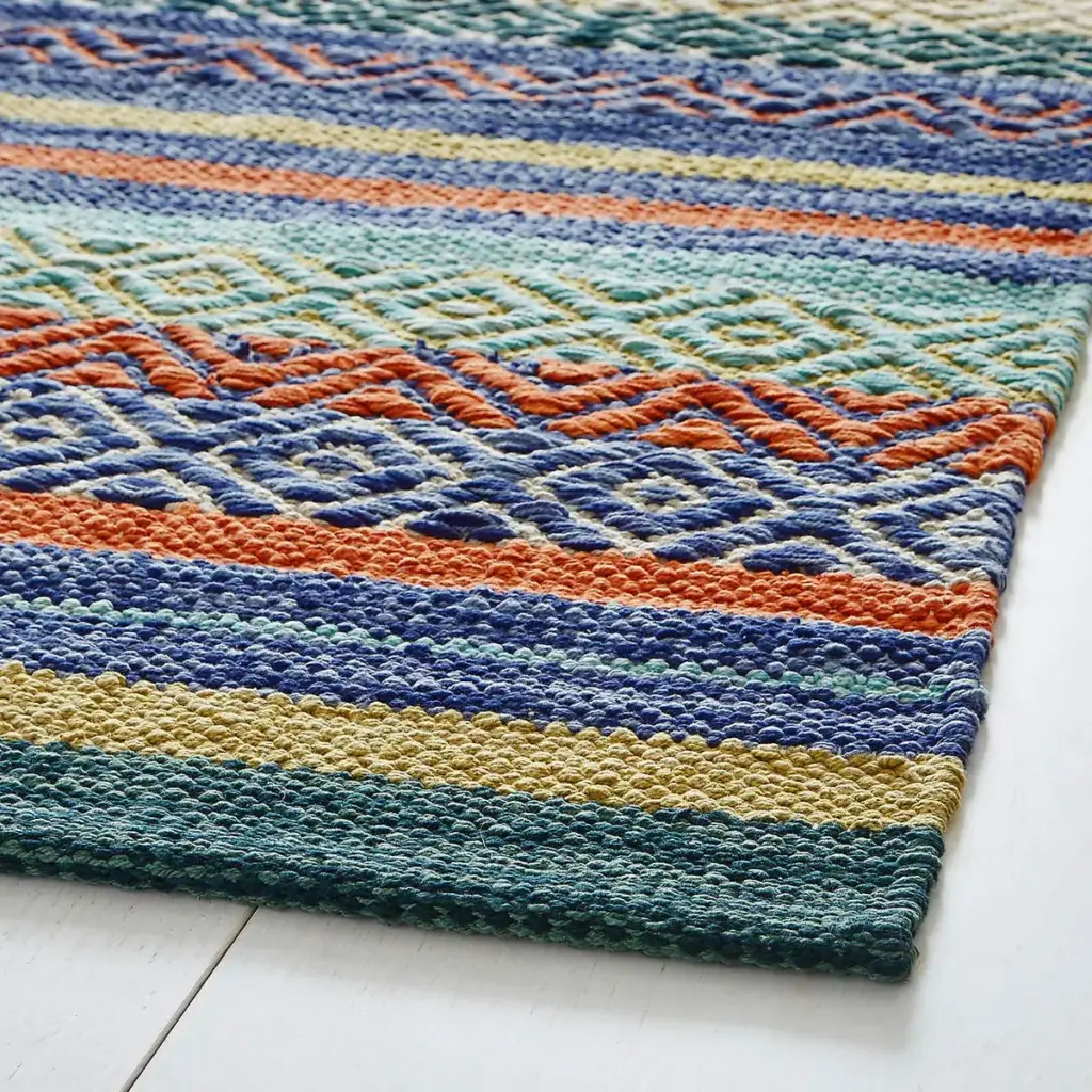 A flat-woven rug featuring rows of colorful striped patterns in blue, orange, green, and yellow tones, displayed on a light wooden floor.