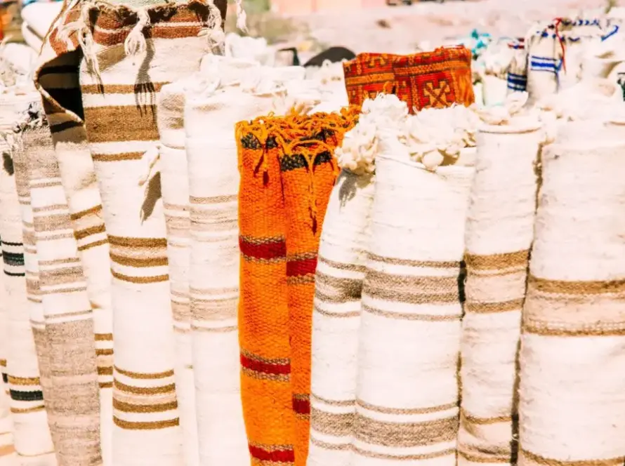 A collection of rolled rugs with striped patterns in natural tones, featuring a bright orange rug with a bold design among neutral-colored ones.