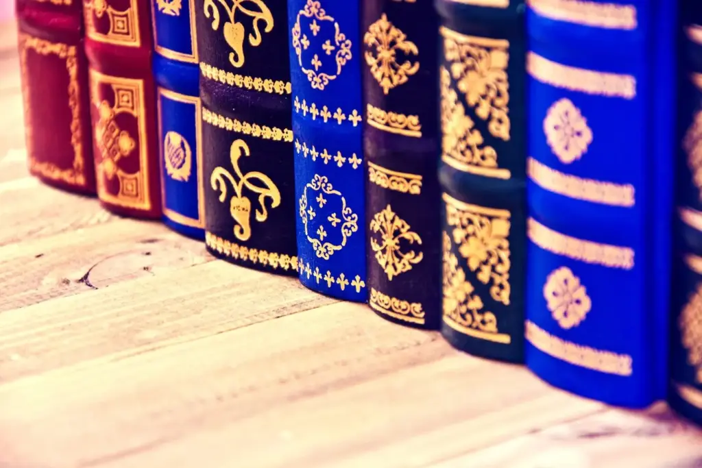 A close-up of a row of vintage books with ornate golden patterns embossed on their spines, displayed on a wooden surface.