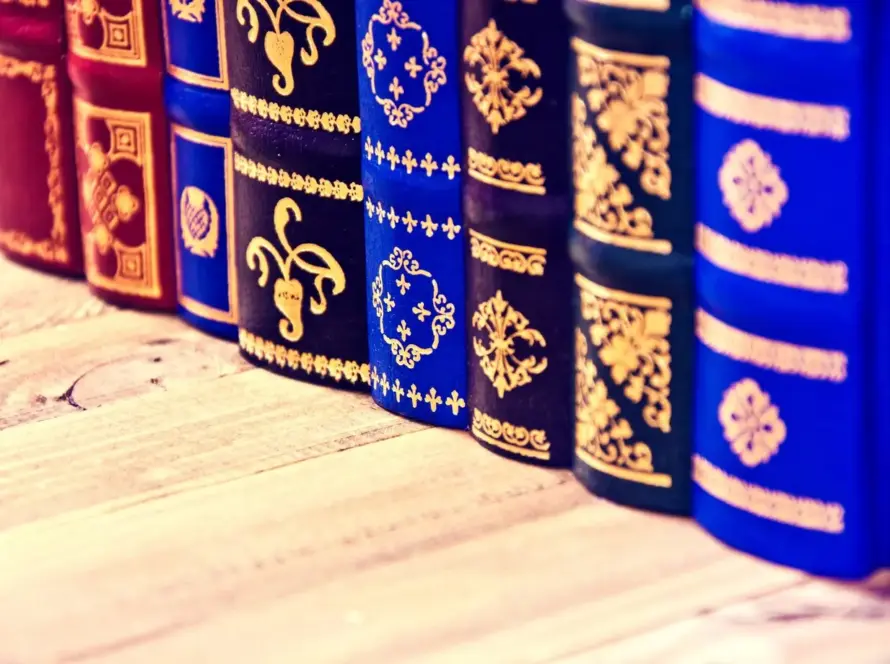 A close-up of a row of vintage books with ornate golden patterns embossed on their spines, displayed on a wooden surface.
